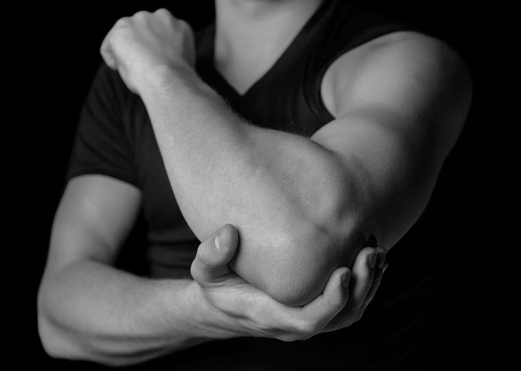 Gray scale image, person holding elbow - What is a Tendon and Why do They Hurt blog post