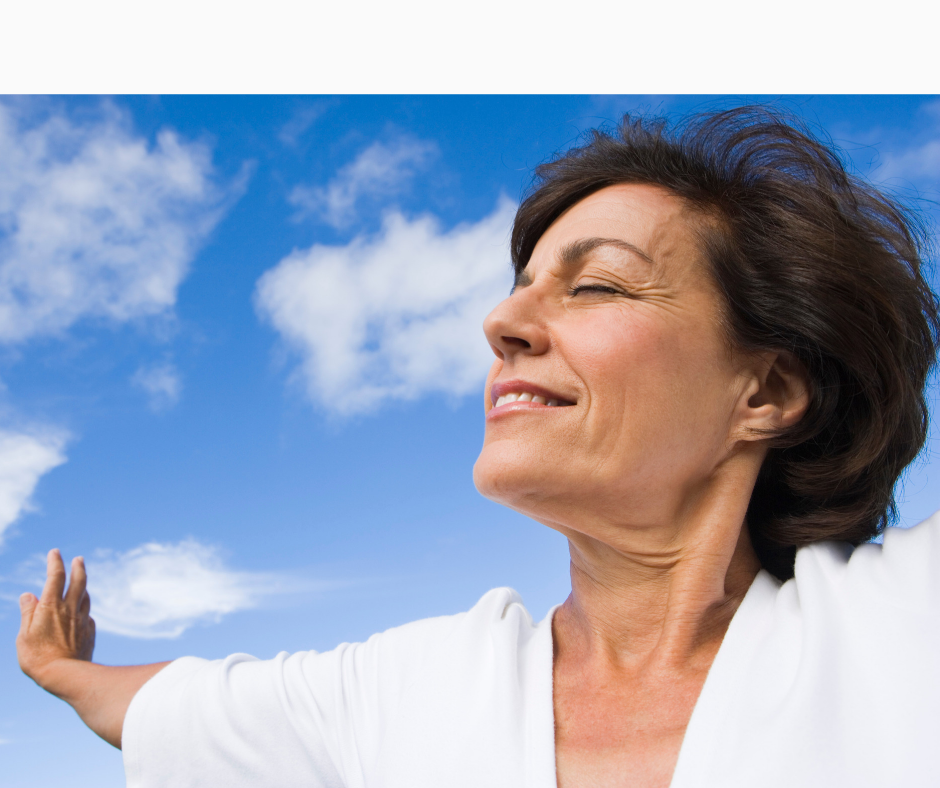 Smiling middle-aged woman outside, eyes closed, outstretched arms